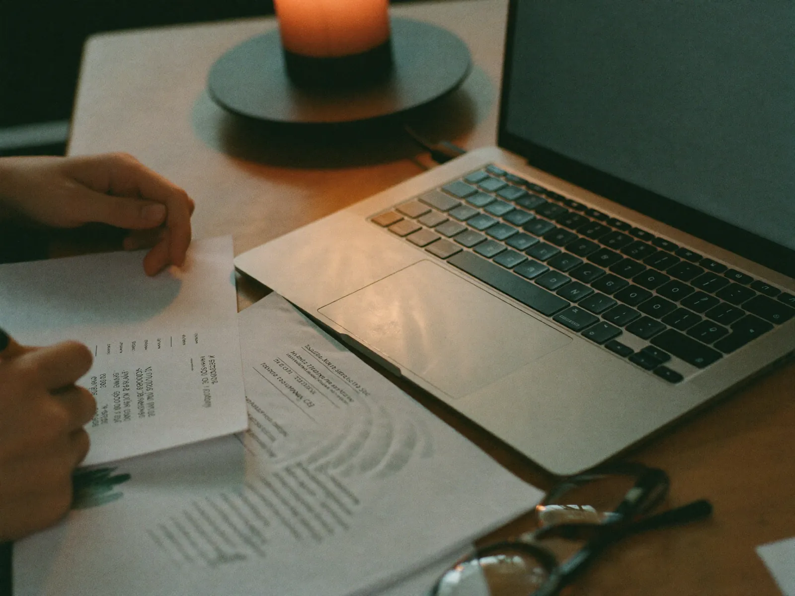 Hands writing notes beside printed statistical tables and a laptop